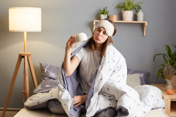 清晨醒来。女人的肖像穿着睡衣躺在床上，裹着温暖舒适的毯子，举着空咖啡杯，需要能量，悲伤和不安。图片下载