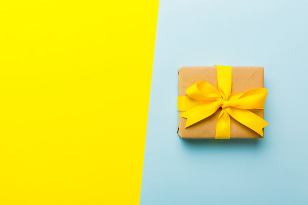 节日纸礼物系黄丝带蝴蝶结顶部视图与复制空间。平铺假日背景。生日或圣诞礼物。圣诞礼盒概念与复制空间图片下载