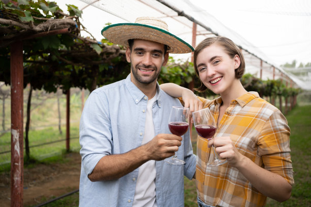 微笑的成年西班牙男子和俄罗斯女子夫妇酿酒师与一杯红酒在葡萄园测试质量。用来酿酒的葡萄种植园。图片下载