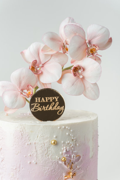 粉色和白色奶油奶酪糖霜点缀的婚礼蛋糕，白色背景上有可食用的兰花糖花和金色花瓣图片下载