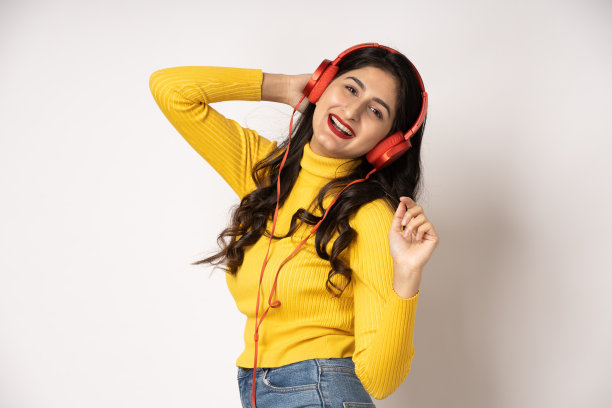 戴着耳机的女人随着她最喜欢的音乐跳舞，在白色的演播室背景上微笑，照片图片下载