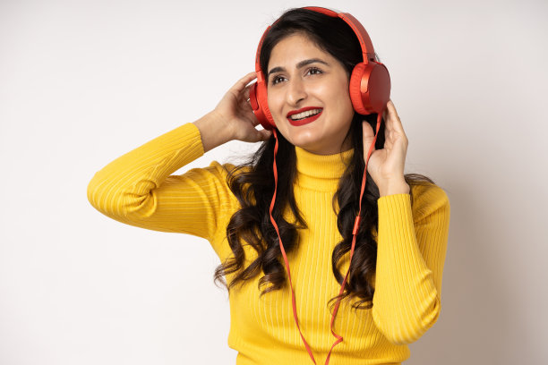 戴着耳机的女人随着她最喜欢的音乐跳舞，在白色的演播室背景上微笑，照片图片下载