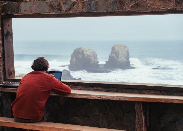 一名男子坐在电脑前看着大海，智利蓬塔·德·洛波斯的皮切勒穆。图片下载