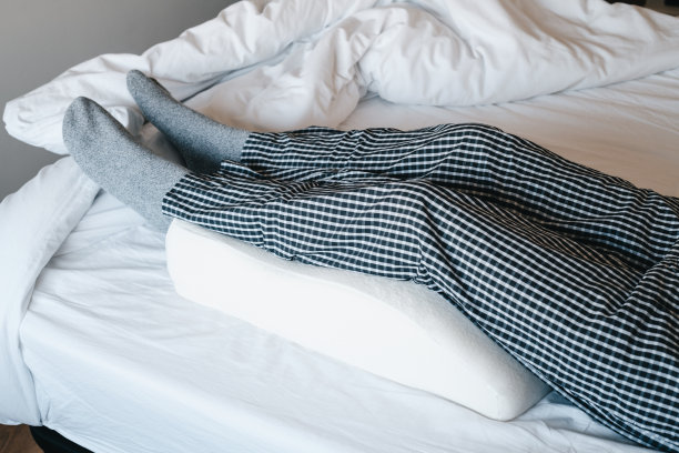 在床上，把腿靠在抬高腿的枕头上图片下载