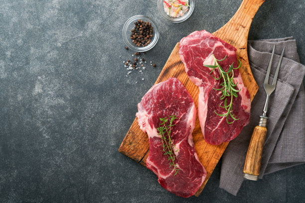 生牛排。大理石生新鲜肋眼牛排与迷迭香，盐和胡椒在砧板上的深色混凝土背景。生牛排和烹饪用香料。图片下载