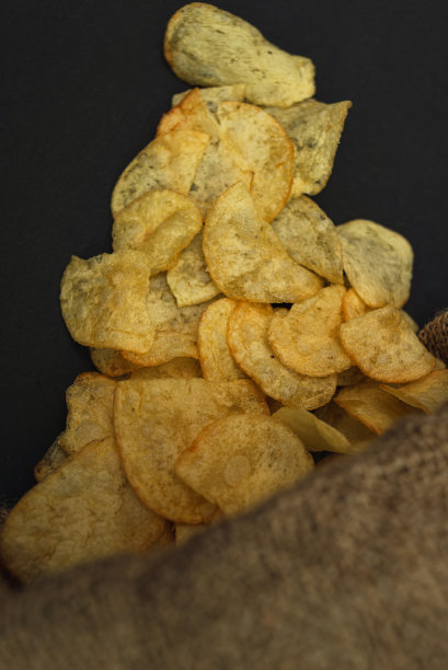 一个装有薯片的帆布袋散落在一张黑色的桌子上。薯片从包里溢出来了图片下载