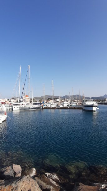 一个码头的照片，美丽的白色小船在水晶蓝色的大海和全景的山脉图片下载