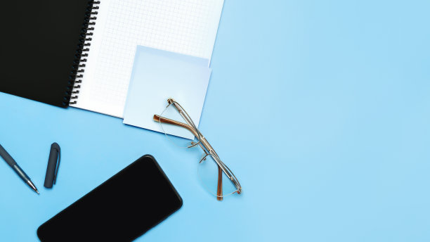平面布局，办公桌面俯视图。工作区有笔记本，智能手机，眼镜，文具，钢笔，蓝色背景。图片下载