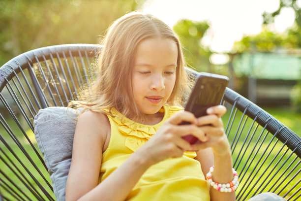 快乐的小女孩在公园玩手机游戏图片下载