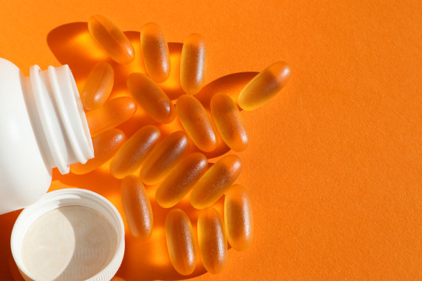 从瓶子里倒出来的欧米茄3胶囊，特写照片，橙色背景。鱼油营养补充顶部视图白色背景。图片下载