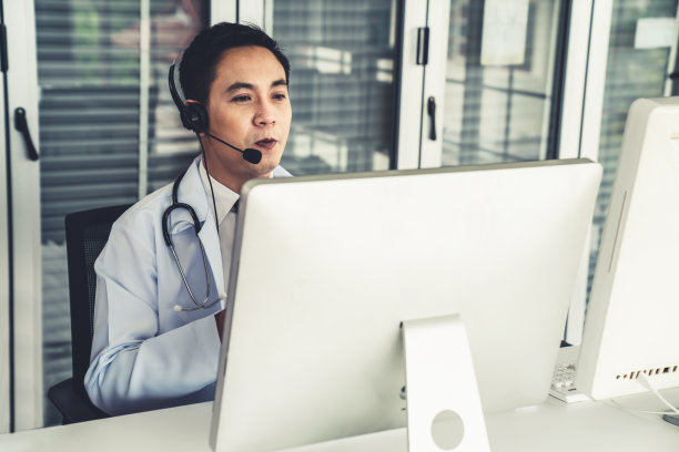 医生戴着耳机在诊所或医院积极视频通话。远程保健和远程医疗服务的概念。图片下载