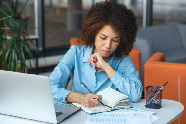 专注于成功的非裔美国女企业家，笔记本电脑，在桌子上工作，在笔记本上做笔记，在一个现代化的办公室里写计划图片下载
