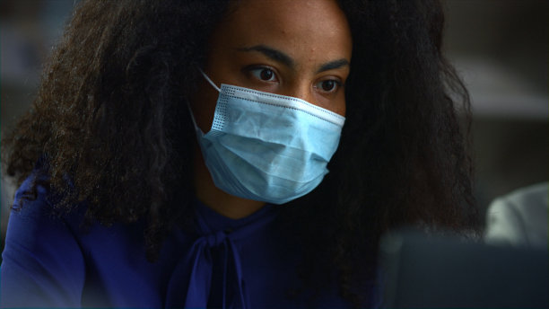 非裔美国女商人戴着面具在办公室搜索笔记本电脑。图片下载