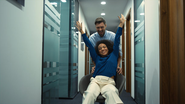 公司团队在走廊公司办公场所竞速办公椅。图片下载