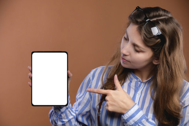 年轻快乐的白人妇女在衬衫和眼镜持有食指笔记本电脑与空白屏幕的工作空间，工作室肖像图片下载