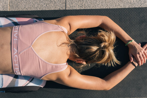 俯拍照片，一位面目全非的运动女子跪在户外的瑜伽垫上，通过身体向前伸展背部、手臂和肩膀。图片下载