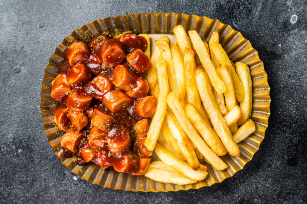 德国咖喱香肠配炸薯条，装在钢板里。黑色背景。俯视图图片下载