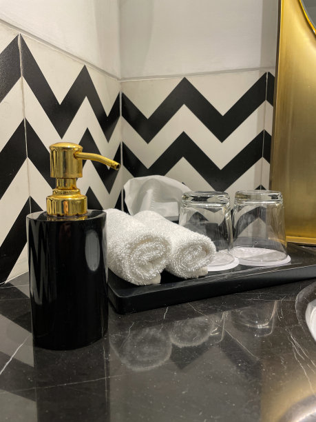 特写图片黑色大理石柜台上的黑色泵式皂液分配器，白色浴室水槽，纸杯上有倒置水杯的大理石托盘，两个卷面法兰绒，豪华浴室里还有一盒纸巾，黑白之字形墙砖图片下载