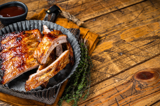 烟熏排骨上了烧烤酱汁，装在钢板里。木制背景。前视图。本空间图片下载