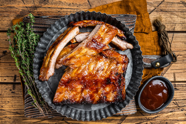 烟熏排骨上了烧烤酱汁，装在钢板里。木制背景。俯视图图片下载