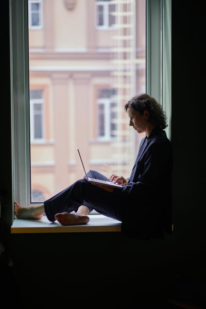 侧面拍摄的女性在商务套装看着笔记本电脑坐在窗户上图片下载