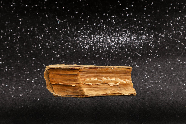 一本破旧的复古书悬浮在闪闪发光的黑色闪闪发光的背景。照片与选择性焦点和复制空间图片下载