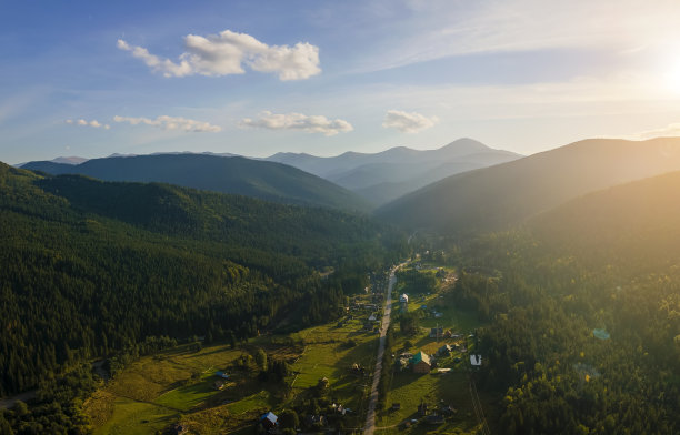 秋天日出时，鸟瞰图上的小村庄房屋在雾蒙蒙的黑暗山峰之间，山顶上覆盖着森林松树。美丽的野生林地，黎明时分的阳光熠熠生辉图片下载
