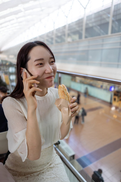 年轻的女商人在机场边吃三明治边打电话图片下载
