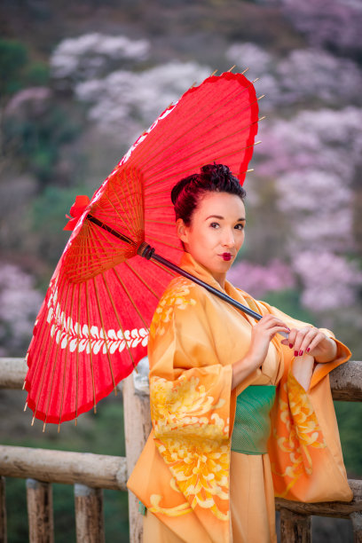 樱花时节，身着橙色和服、打着红色雨伞的女子图片下载
