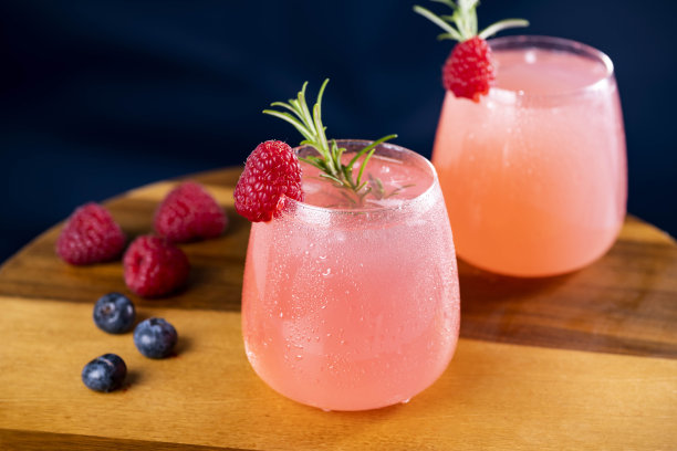 粉红色鸡尾酒在玻璃杯，装饰迷迭香，覆盆子和蓝莓库存照片图片下载