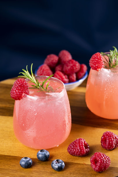 粉红色鸡尾酒在玻璃杯，装饰迷迭香，覆盆子和蓝莓库存照片图片下载