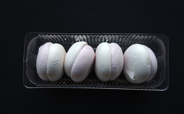 白色和粉红色的棉花糖在黑色的背景上。塑料包装的棉花糖。喝茶时吃的甜点心。图片下载