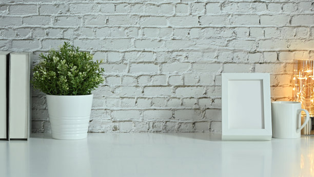 靠砖墙的白桌上摆放着空画框、盆栽、书籍和咖啡杯。图片下载