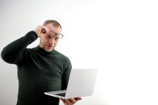 成年男子拿着笔记本电脑，抬起眼镜，他很惊讶恢复视力眼药水戴上眼镜胡须酒窝脸颊白底胡子网上学习购物在电脑前工作图片下载