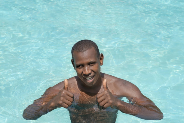 运动员在阳光下的游泳池里微笑，竖起大拇指(享受他的假期，照片图片下载