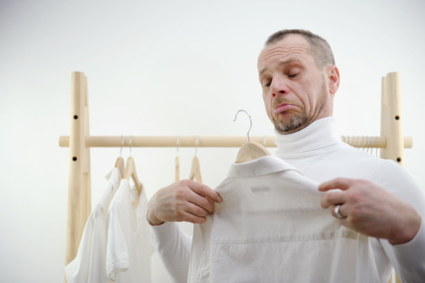 男人对着木衣架的背景做鬼脸，试图把衬衫穿在自己身上，不喜欢甚至皱着眉头，闭着眼睛，手环的概念，选择衣服，剪裁，清洗，洗衣图片下载