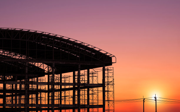 在日落的天空背景下，建筑工地的弧形屋顶工业建筑结构剪影图片下载