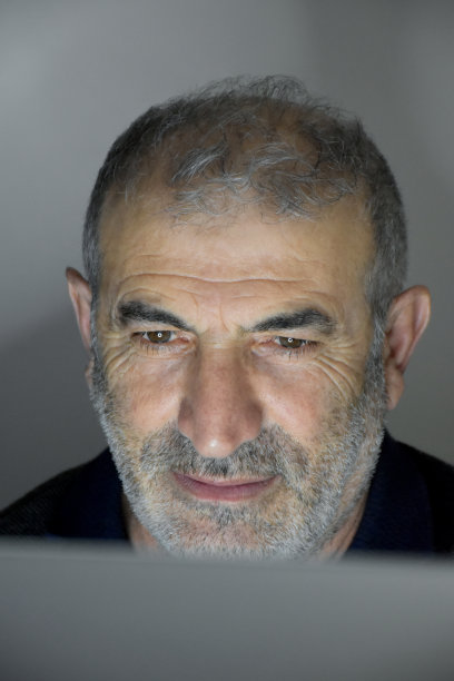 高级男子在电脑上工作，屏幕在他的脸上反射在晚上图片下载