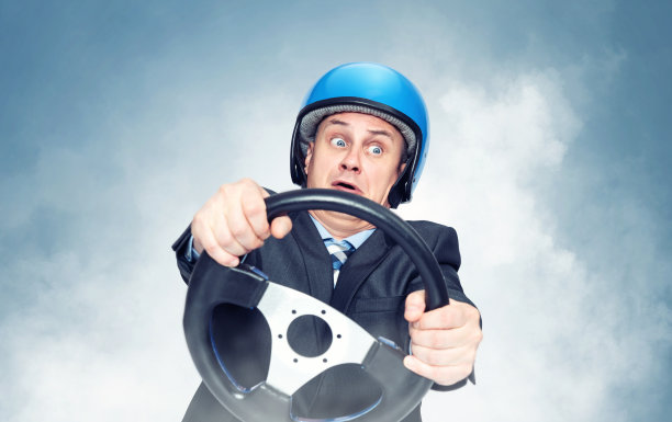 一名身穿深色西装、戴着摩托车头盔的男子在转弯时手里握着汽车方向盘，背景是蓝色的烟雾图片下载