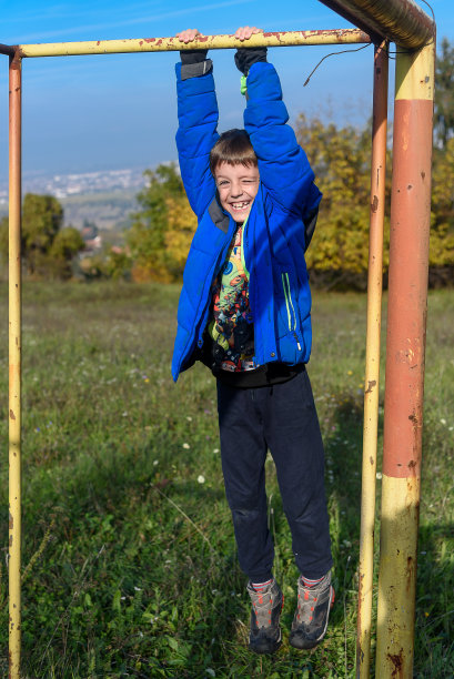 孩子们在运动场上做引体向上。男孩在户外做引体向上。这个男孩正在做引体向上图片下载