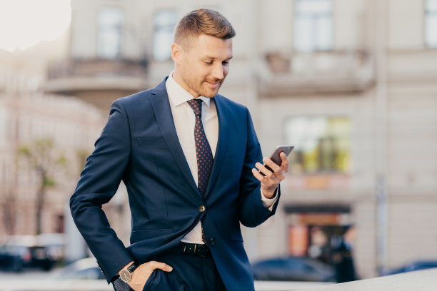 照片中，成功的男性企业家手里拿着现代智能手机，阅读金融交易所的新闻，浏览互联网，在线支付，休息，去咖啡馆或餐厅图片下载