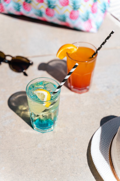 泳池边的热带气泡柠檬水鸡尾酒，粉红色的沙滩包和白色的帽子作为背景。玻璃杯的图片与橘子和薄荷柠檬水果。你好，暑假假期图片下载