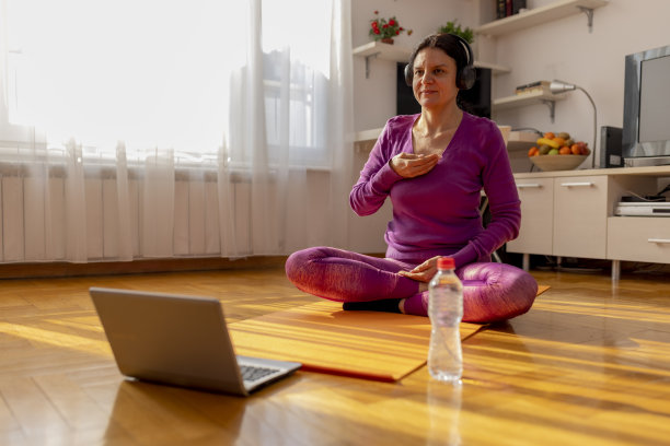 美丽的女人在家里练习瑜伽，坐在瑜伽垫上冥想，微笑放松。图片下载