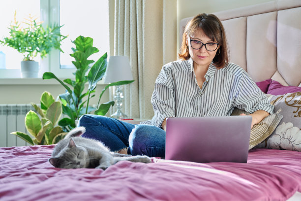 中年妇女在家里的床上，笔记本电脑和猫图片下载