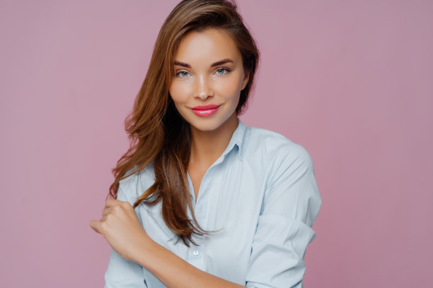 肖像令人愉快的女模特与深色长发，自信地看着相机，有化妆，微笑温柔，姿势使照片杂志封面，孤立在紫色背景。图片下载