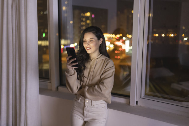 年轻女子在夜间使用智能手机的正面视图，背景是城市景观图片下载