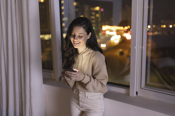 年轻女子在夜间使用智能手机的正面视图，背景是城市景观图片下载