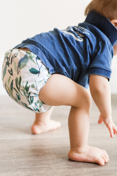 一个一岁大的男孩在地板上玩耍，学习走路，只穿着叶子图案的布尿布和蓝色衬衫图片下载