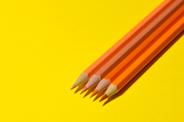 橙色铅笔在明亮的黄色背景上带有刺眼的阴影。文本空间图片下载
