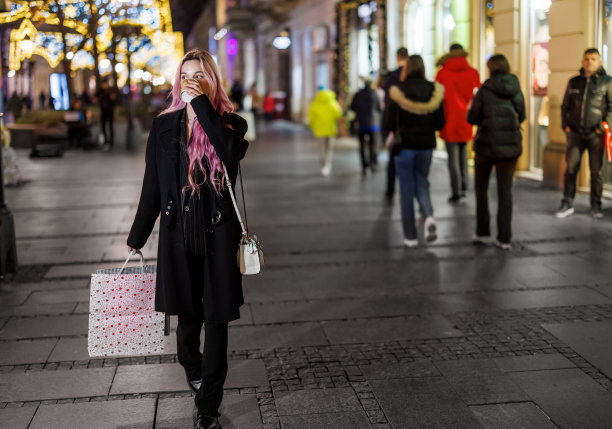 一个女人提着纸袋走在市区，享受着购物的乐趣。图片下载
